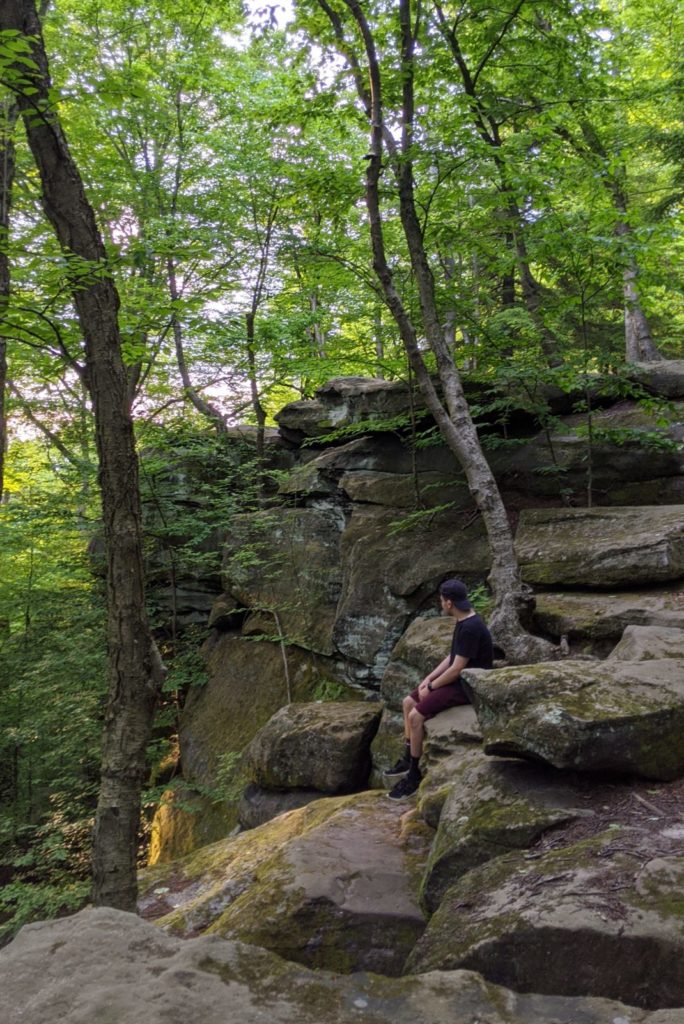 A person sits, looking away, on large rock formations in CVNP.