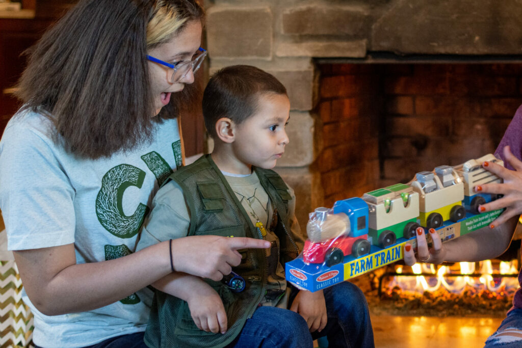 Girl and boy look at toy train near fireplace