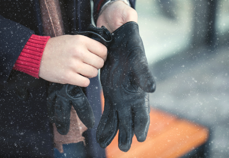 Stock photo of man putting on winter gloves outside while it's snowing