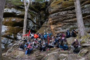 A group of women posing on rocks in the park, some with their hands up.