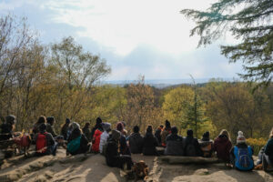 A group of people sit with their backs toward the camera. They sit lining the edge of the ledges overlook.
