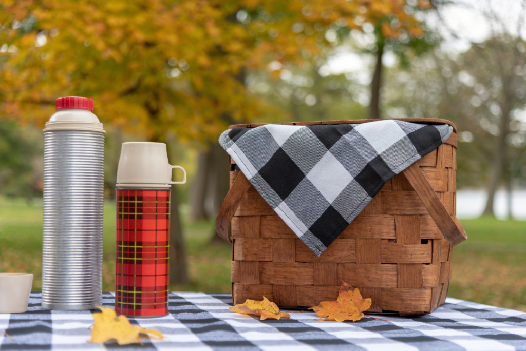 Picnic basket and thermoses on a picnic table in a park in fall