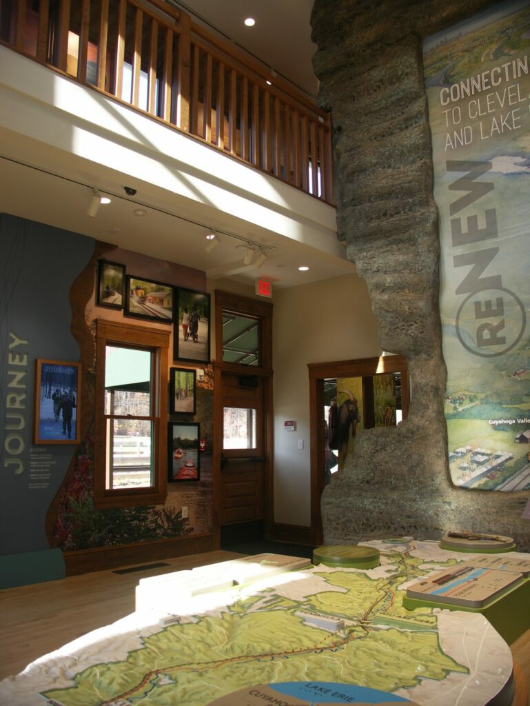 A tabletop relief map of Cuyahoga Valley National Park is opposite an informational wall with screens displaying photographs of the park. 