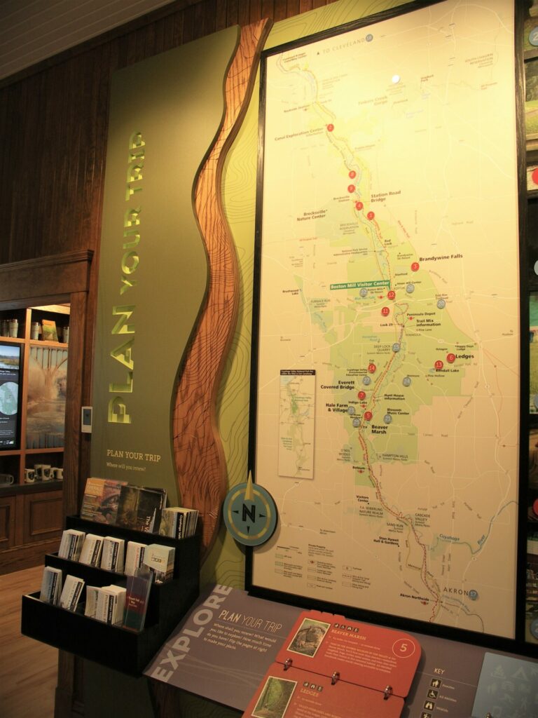 Wall signage reads Plan Your Trip. Next to the signage us a large map of the park with markers for popular attractions and trails. Next to the map is a tiered display holder for free take-along park maps and brochures. 