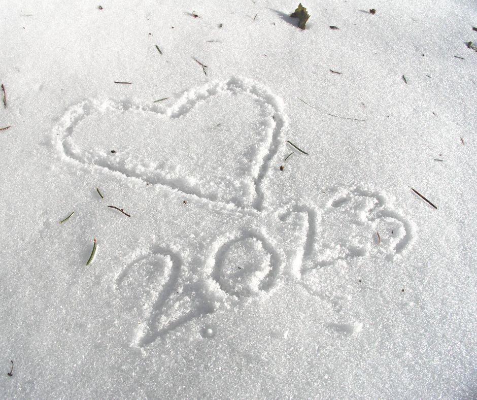 A close-up of snow on the ground is shown. Several loose evergreen needles are resting on the snow. The shape of a heart and the number 2023 are etched into the snow.