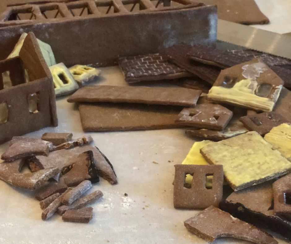 Discarded gingerbread pieces are piled up on a flour-dusted piece of parchment paper. The shapes include pieces from a gingerbread house frame, chocolate-iced roof pieces, and a version of the Station Road bridge turned on its side. Some of the pieces are iced in a pale-yellow icing the color of the Brecksville Train Station. 