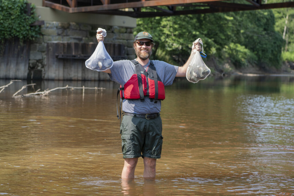 Ryan Trimbath, park biologist, holds up bags of mussels in the Grand River that have been deemed not right for the experiment and have been put back in the Grand River where they came from.