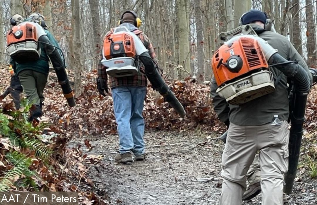 A photo of three volunteer workers using leaf blowers on a wooded trail.
