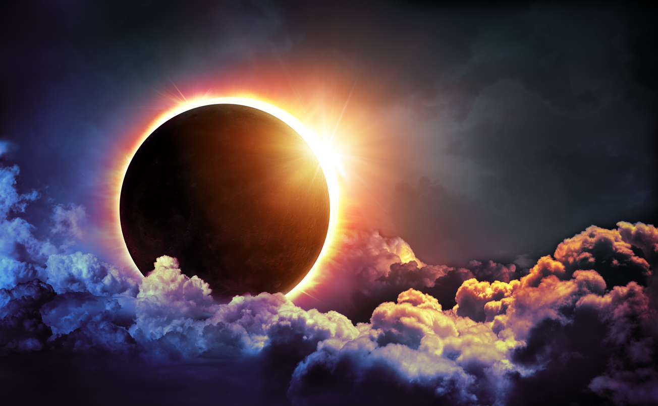 An image of a solar eclipse where the moon is covering most of the sun. A dark sky and purple, red, and yellow-hued clouds surround the sun.