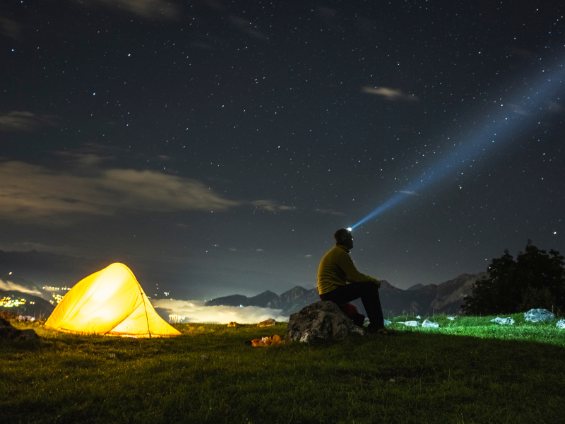 Dark sky with person sitting on a rock with a headlamp on looking up at sky.