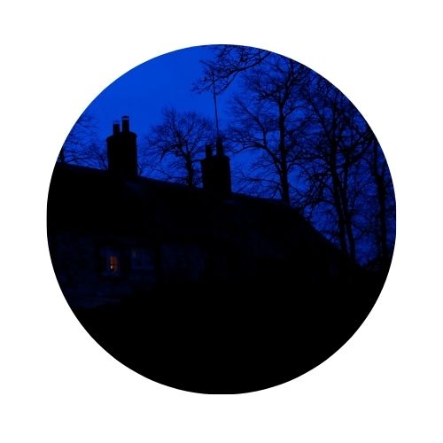 A circular photo of a dark silhouette of a house and trees. 