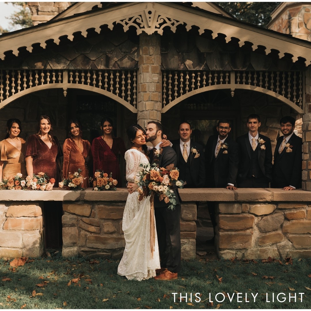 An image of a bride and groom in from of their wedding party and a stone cottage with ornate wooden eaves.