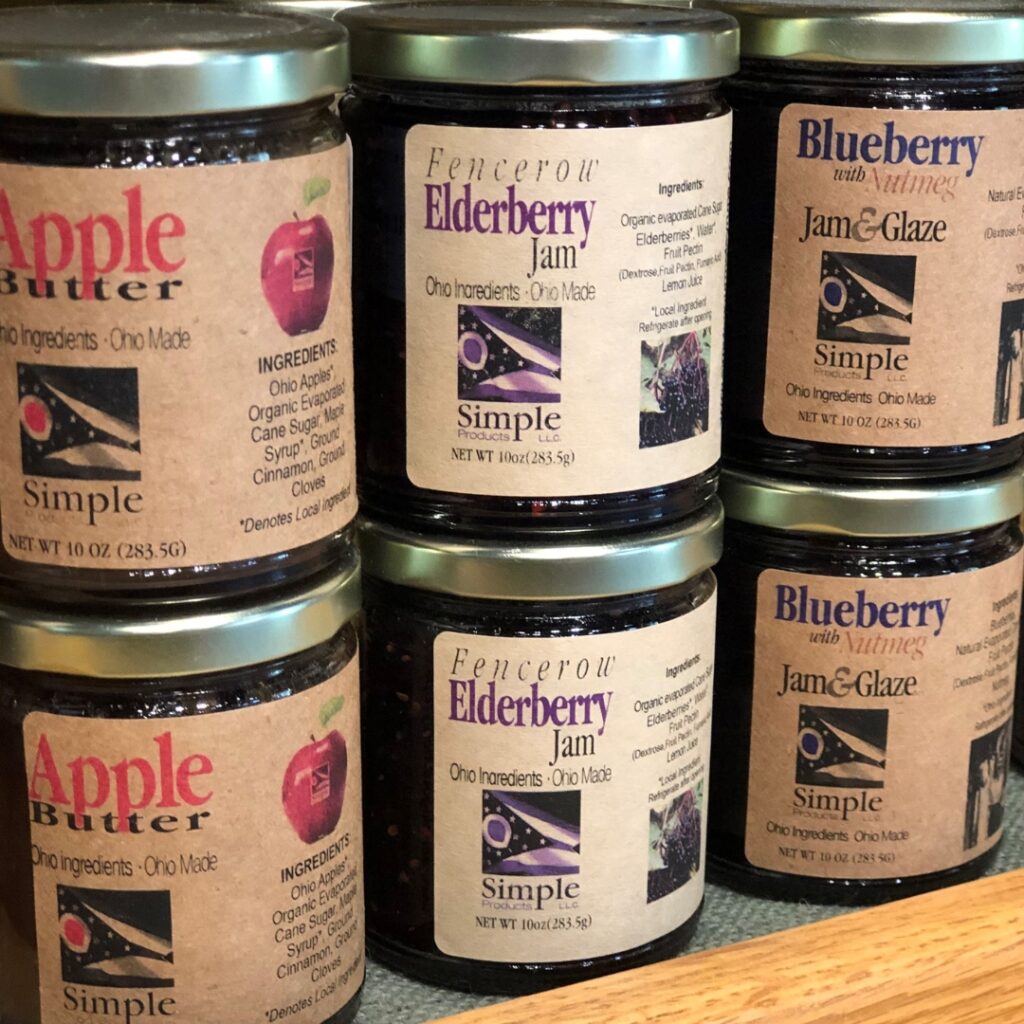 A photo of six jars of fruit spreads. Two are apple butter, two are elderberry jam, and two are blueberry jam and glaze.