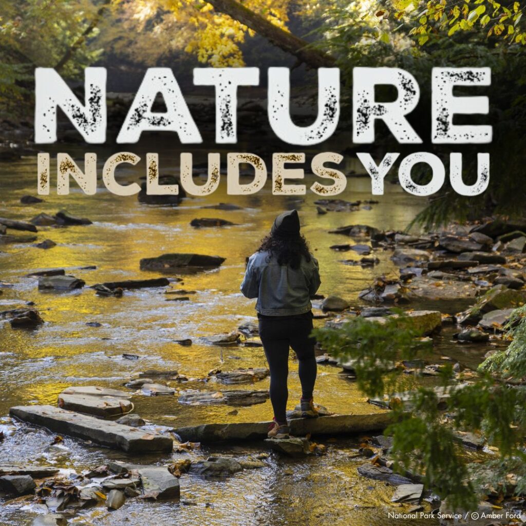 Nature Includes You Logo in forefront of a person standing on a rock in the river.