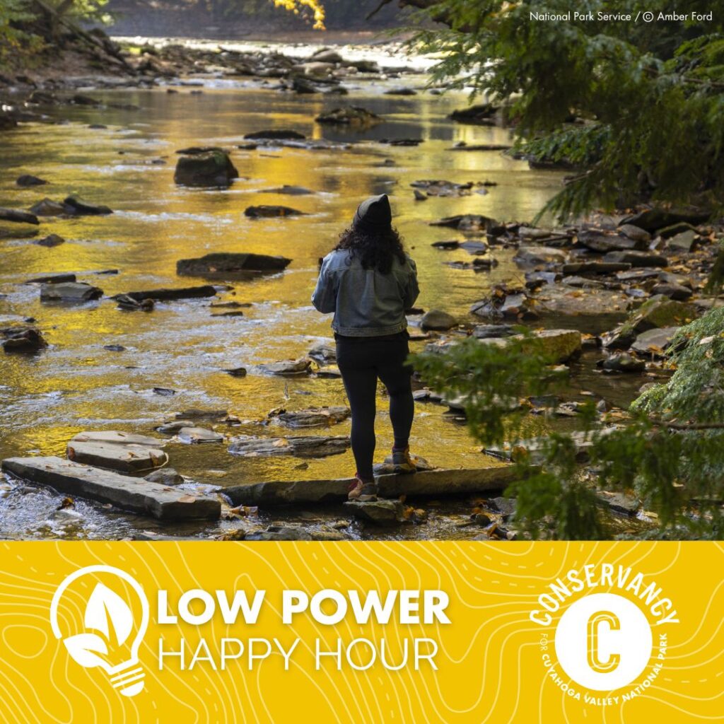 A photo of a woman standing on a rock in a riverbed. Beneath is a logo for Low Power Happy Hour and a logo for the Conservancy for Cuyahoga Valley National Park.
