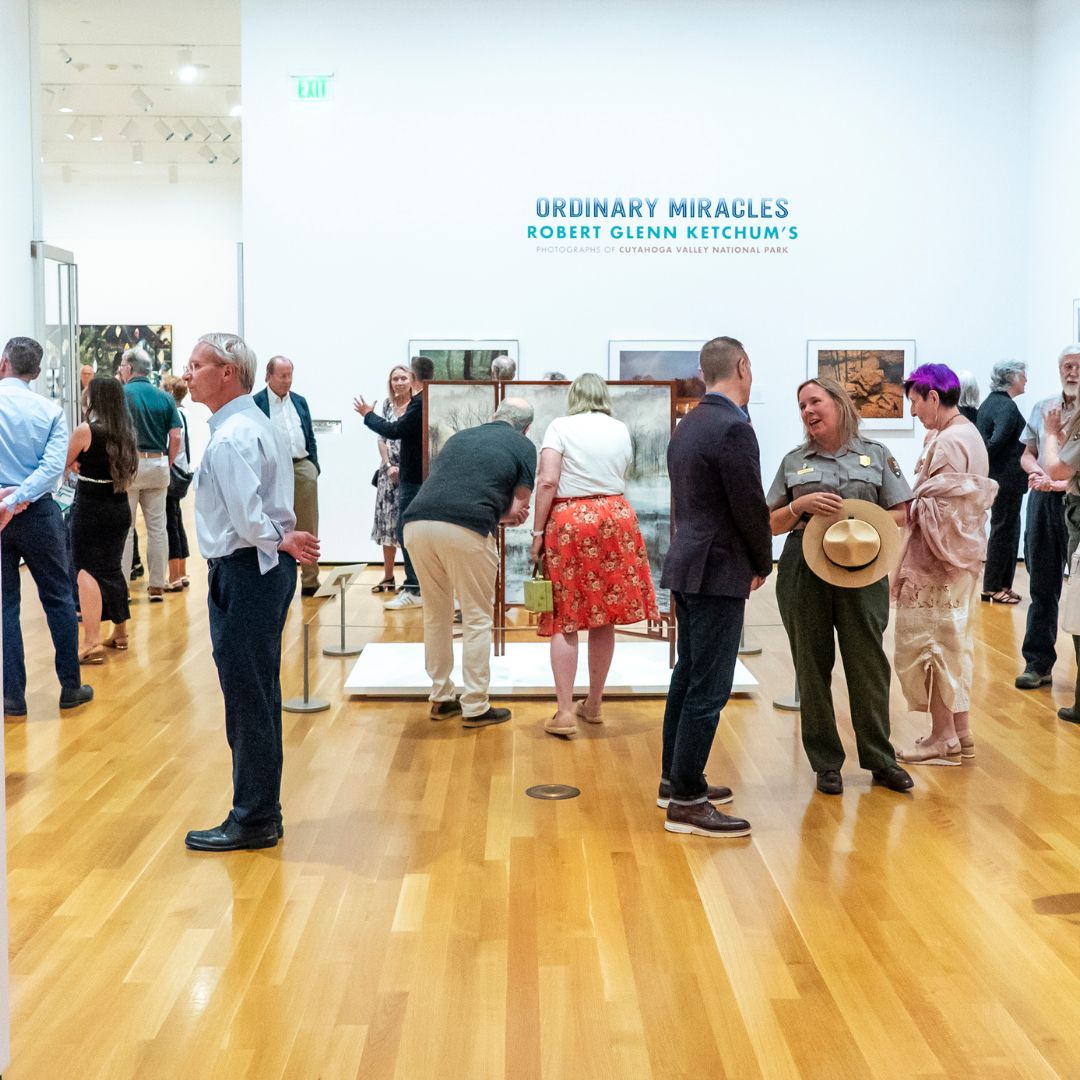 A photo of a gallery at the Akron Art Museum. People are standing in the gallery, which has an installation of artwork and photography by artist Robert Glenn Ketchum.