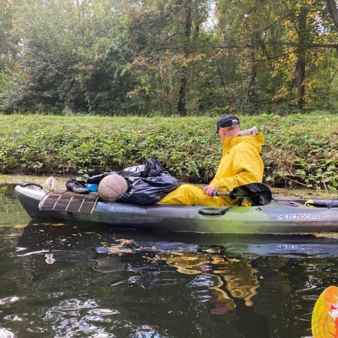 A photo of a person on a kayak collecting trash found in or by a river.